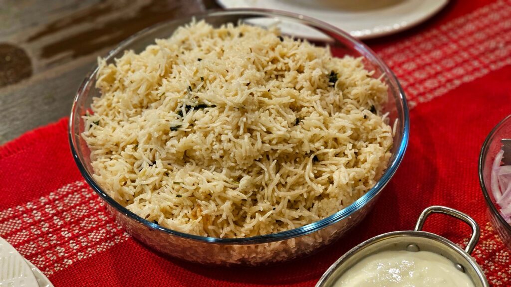 Un bol de riz basmati parfaitement cuit, servi avec du yaourt sur une nappe rouge.