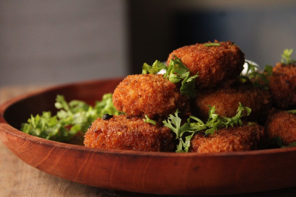 De délicieuses croquettes frites croustillantes, garnies d'herbes fraîches, servies sur une assiette rustique en bois.