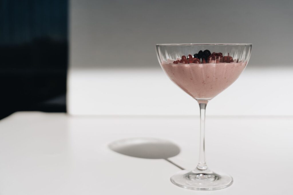 Un dessert rose sophistiqué garni de baies dans un verre ensoleillé, idéal pour se rafraîchir.