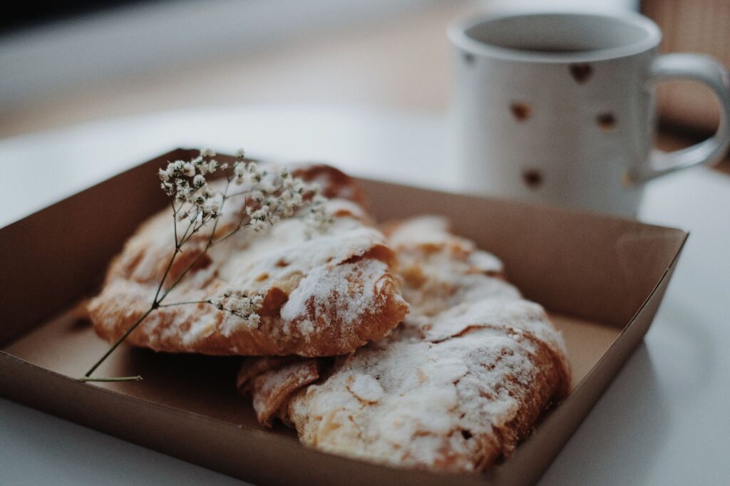 Une paire de croissants saupoudrés de sucre à côté d'une tasse de café dans un cadre intérieur détendu.