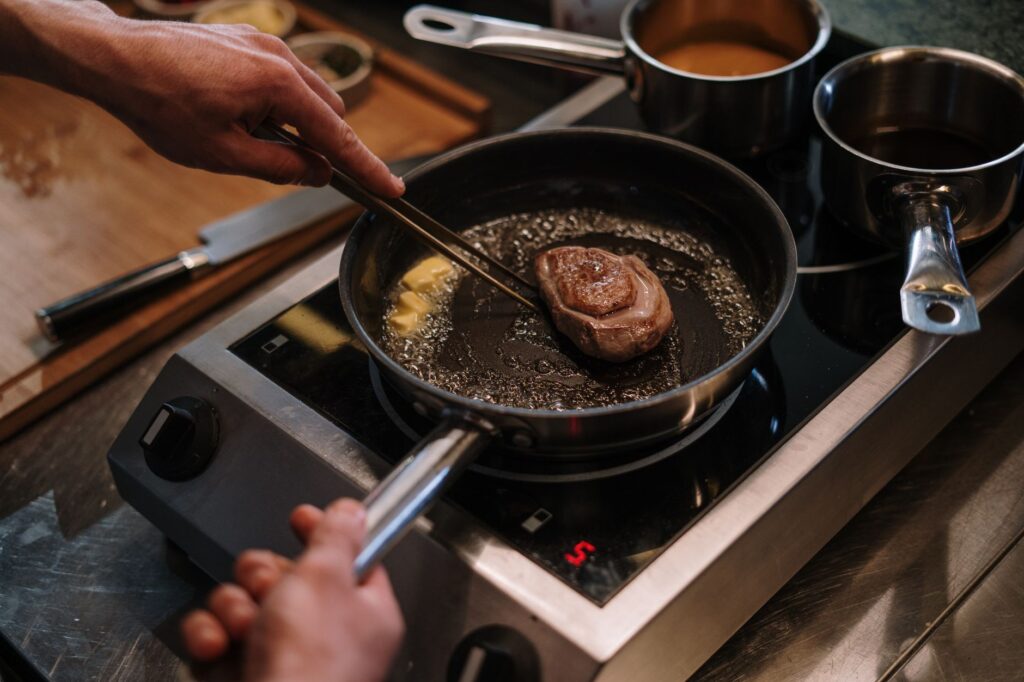 Gros plan sur un steak poêlé dans un cadre de cuisine avec des mains impliquées, capturant l'art culinaire.
