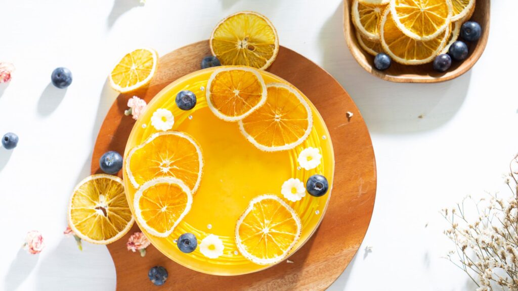 Vue du dessus d'un gâteau au fromage orange vibrant décoré de fruits frais et de fleurs.