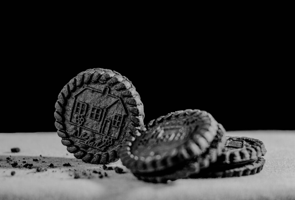 Photographie artistique en noir et blanc de biscuits ronds au chocolat avec un design texturé, sur fond noir.