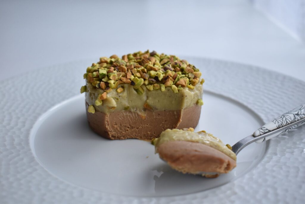 Dessert crémeux garni de pistaches sur une assiette blanche, prêt à être savouré.