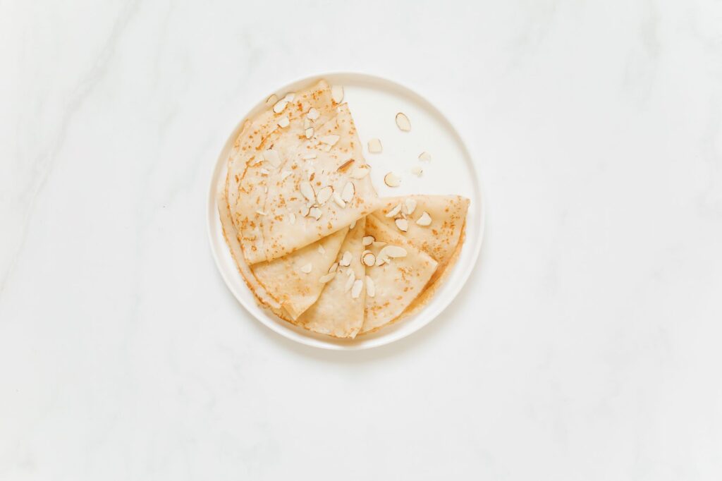 Délicieuses crêpes maison garnies d'amandes tranchées sur une assiette blanche, parfaites pour une douceur.