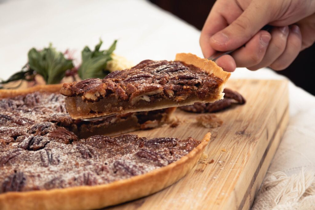 Gros plan sur une tranche de tarte aux noix de pécan faite maison en train d'être retirée d'une planche en bois.