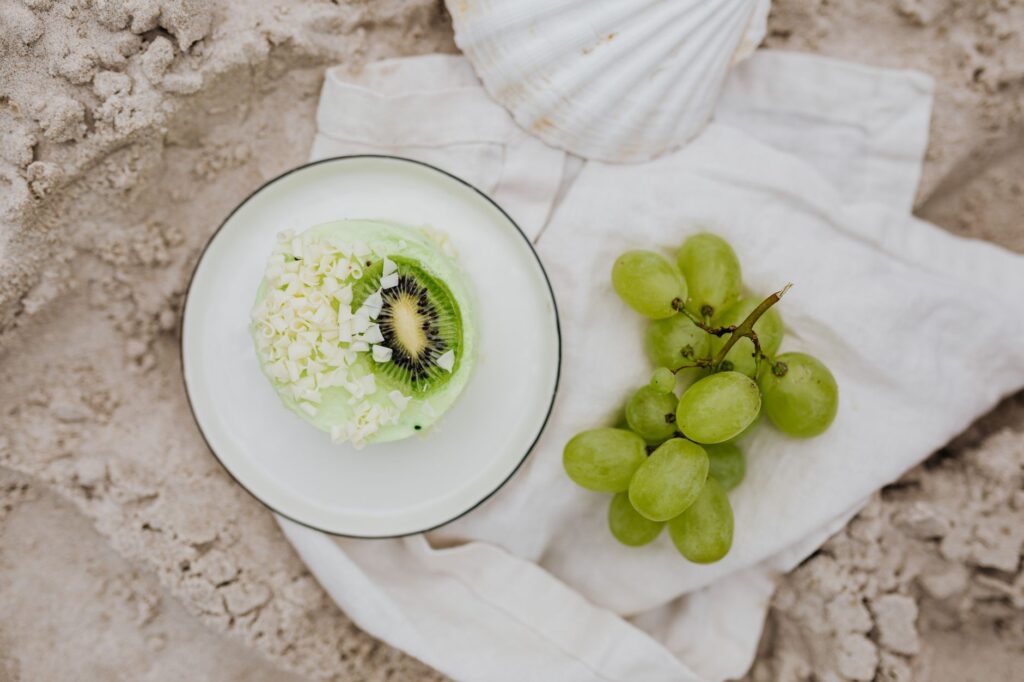 Dessert frais de kiwi et de raisin stylisé contre un fond de plage de sable, évoquant une sensation de détente estivale.