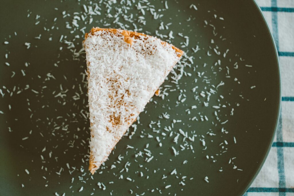 Délicieuse tranche de gâteau garnie de flocons de noix de coco sur une assiette noire, parfaite pour les amateurs de dessert.
