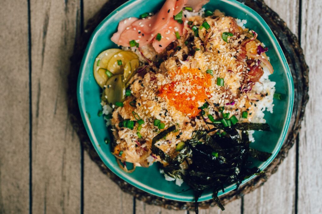 Bol poke coloré avec du riz, du poisson et des légumes frais présenté sur une table en bois rustique.