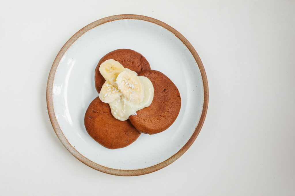Vue de dessus de crêpes avec des tranches de banane et de la crème sur une assiette en céramique.