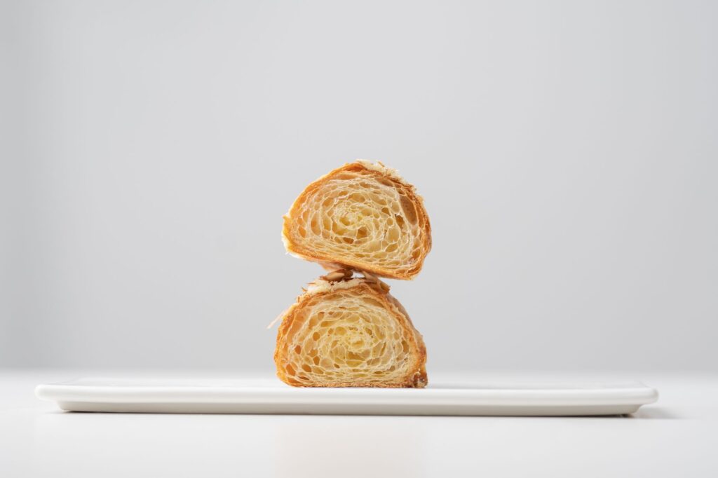 Image minimaliste d'un croissant tranché empilé sur une assiette blanche, mettant en valeur sa texture feuilletée.