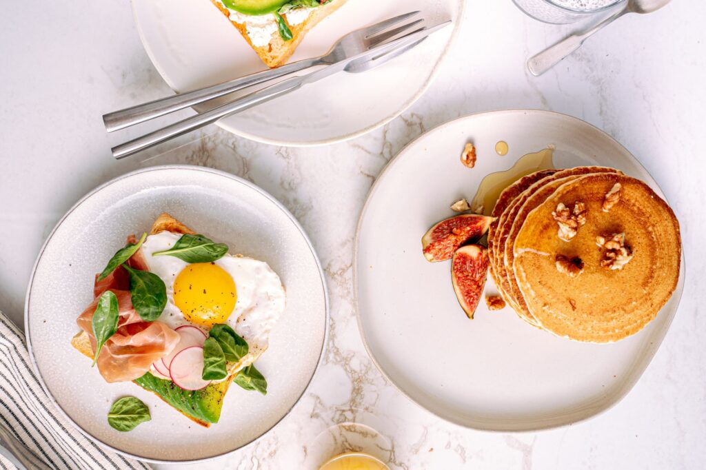 Vue de dessus de plats de petit-déjeuner avec des crêpes et du pain toasté, des œufs et des légumes.