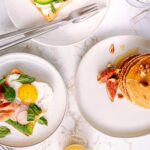 Vue de dessus de plats de petit-déjeuner avec des crêpes et du pain toasté, des œufs et des légumes.