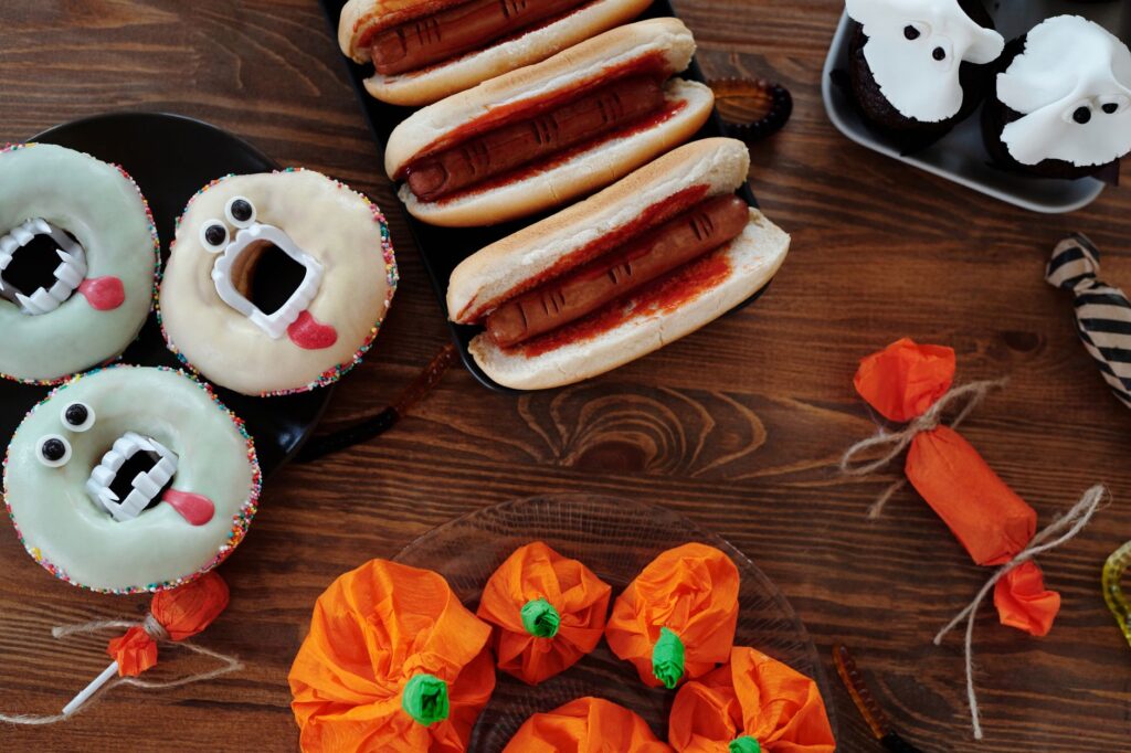 Friandises sur le thème d'Halloween, y compris des donuts, des hot-dogs et des cupcakes présentés sur une table en bois.