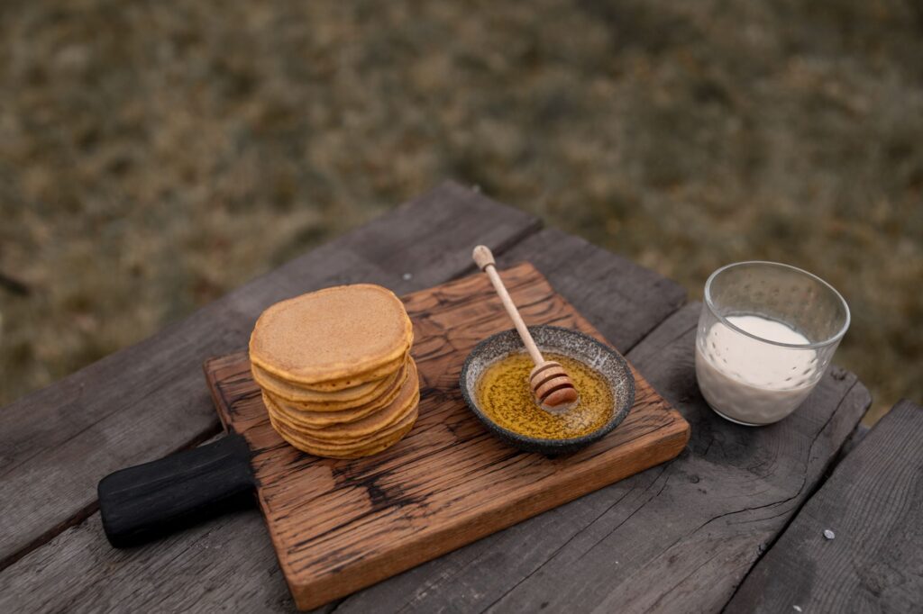 Une pile de crêpes avec du miel et du lait sur une table en bois rustique.