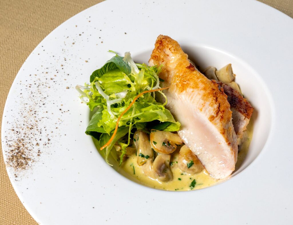 Délicieux plat de poulet avec des champignons et de la salade sur une assiette blanche. Parfait pour les amateurs de cuisine gourmet.