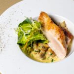 Délicieux plat de poulet avec des champignons et de la salade sur une assiette blanche. Parfait pour les amateurs de cuisine gourmet.