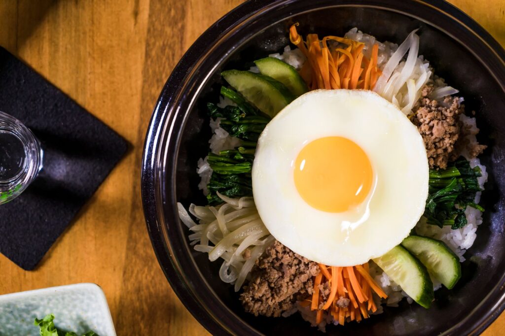 Délicieux plat coréen Bibimbap avec un œuf au plat, des légumes frais et du bœuf savoureux, parfait pour le déjeuner ou le dîner.