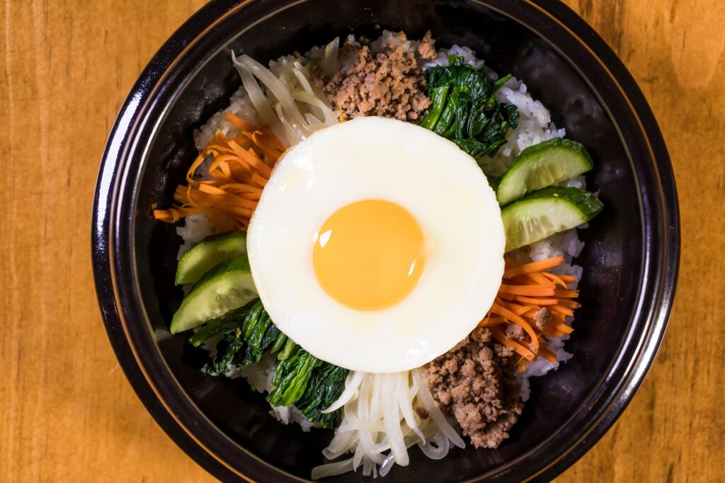 Gros plan sur le Bibimbap coréen avec œuf, riz et légumes frais présentés dans un bol.
