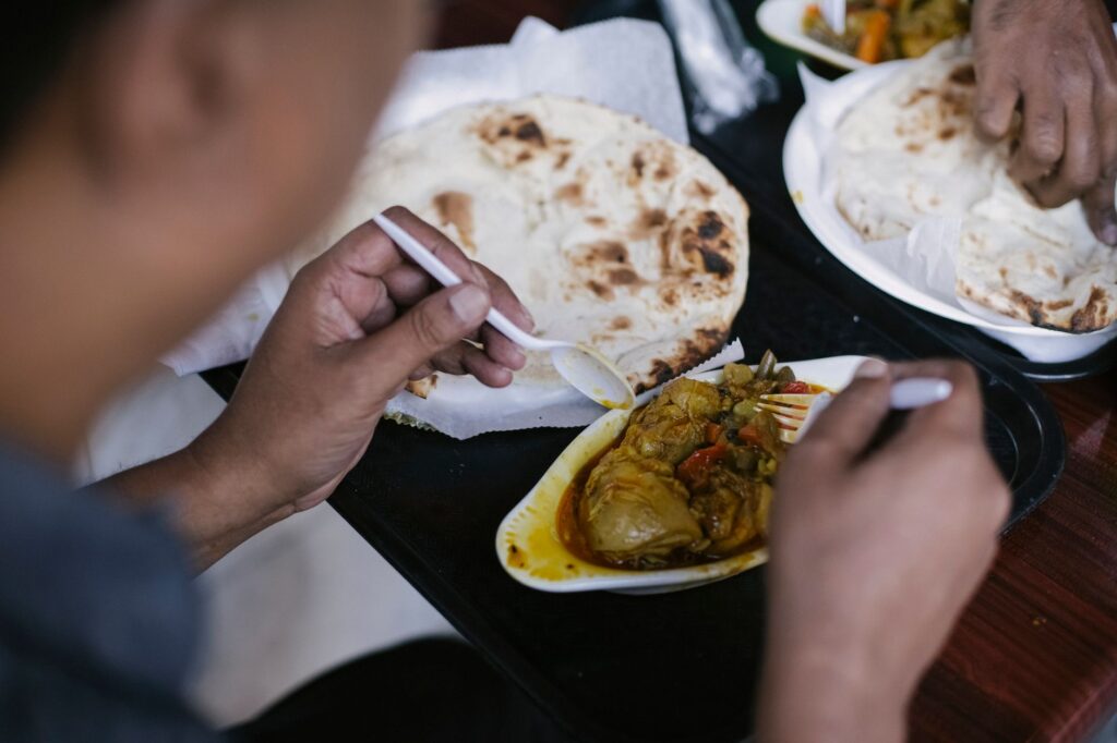 Une personne savourant un plat de curry savoureux avec du pain naan, utilisant des couverts jetables dans un cadre de restauration.