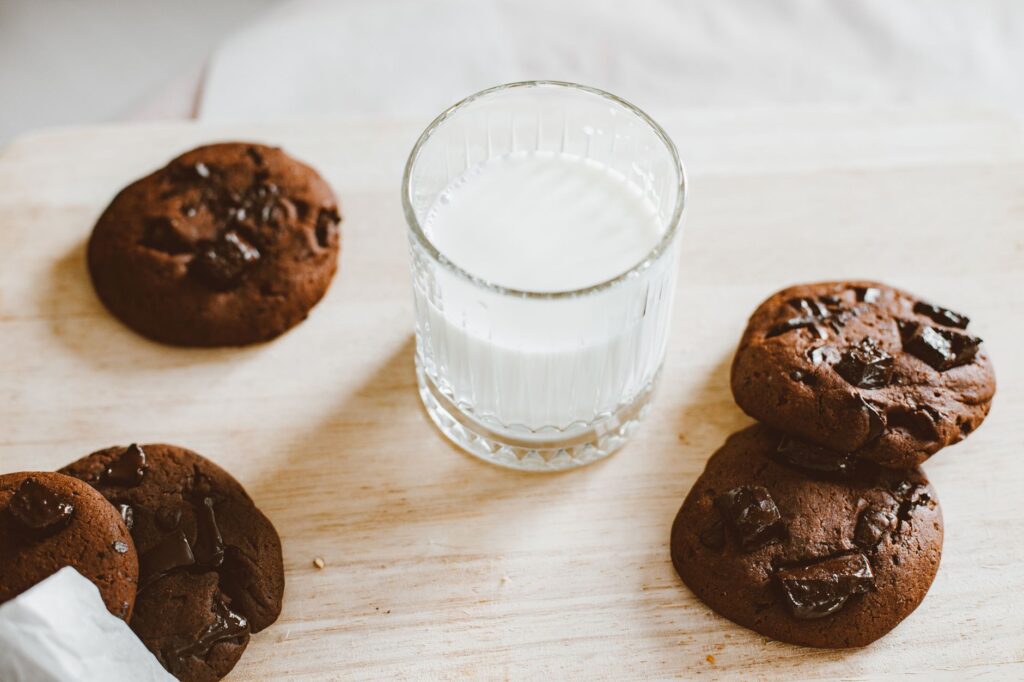 De délicieux cookies aux pépites de chocolat et un verre de lait sur une planche en bois, parfaits pour une douceur.