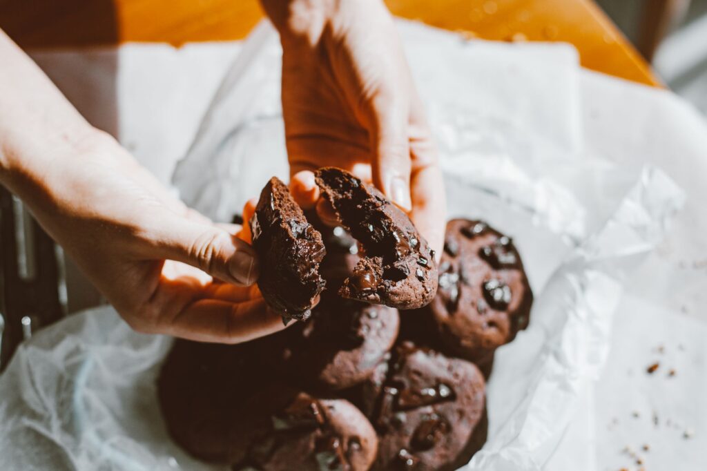 Gros plan sur des mains cassant un délicieux cookie aux pépites de chocolat avec d'autres cookies en arrière-plan.