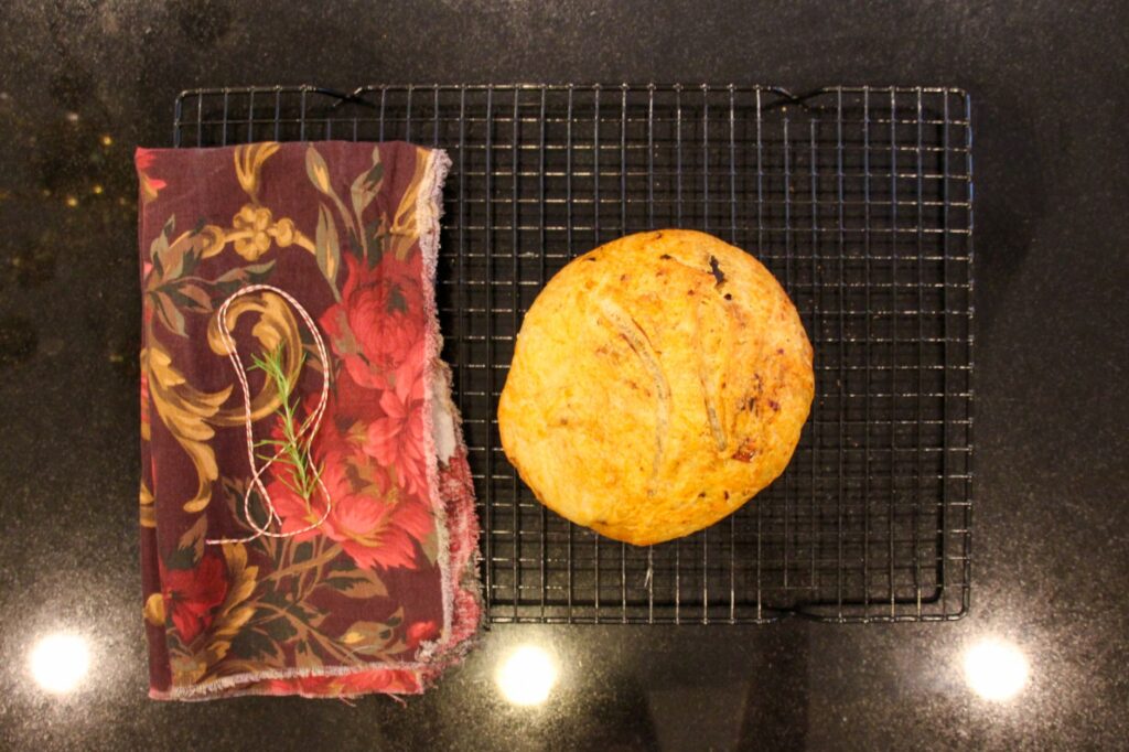 Pain rond fraîchement cuit sur une grille de refroidissement avec une écharpe florale et une garniture d'herbes.
