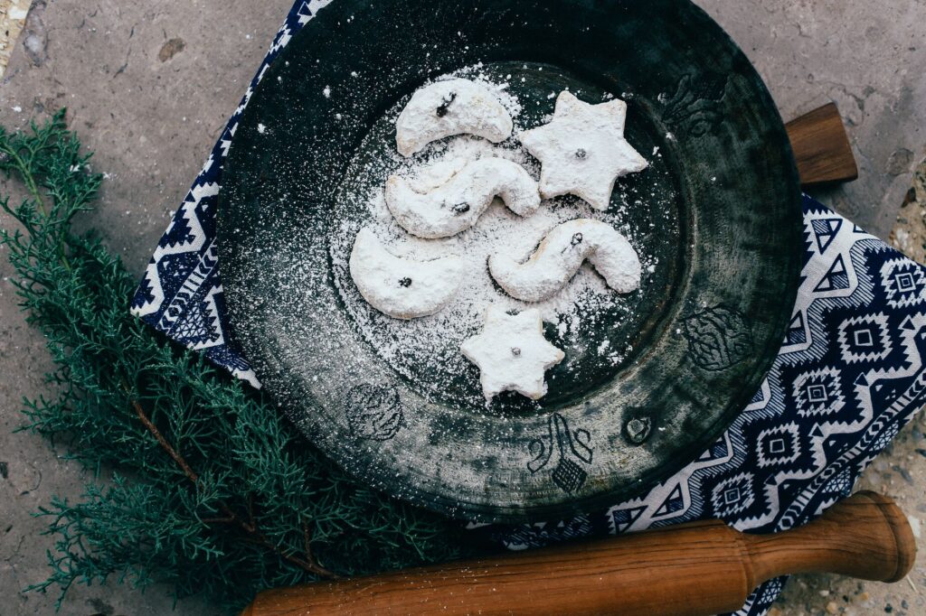 Gros plan de biscuits en forme d'étoile et de croissant saupoudrés de sucre sur une assiette rustique. Parfait pour des thèmes de fêtes.