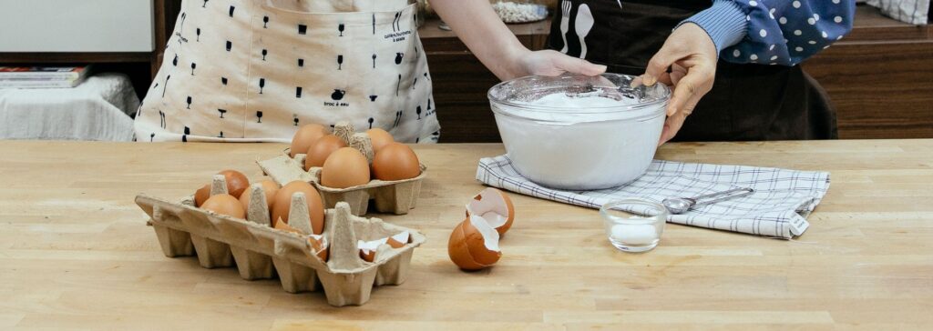 Deux femmes préparant une pâte avec des œufs, de la farine et du sucre sur un plan de travail en bois.