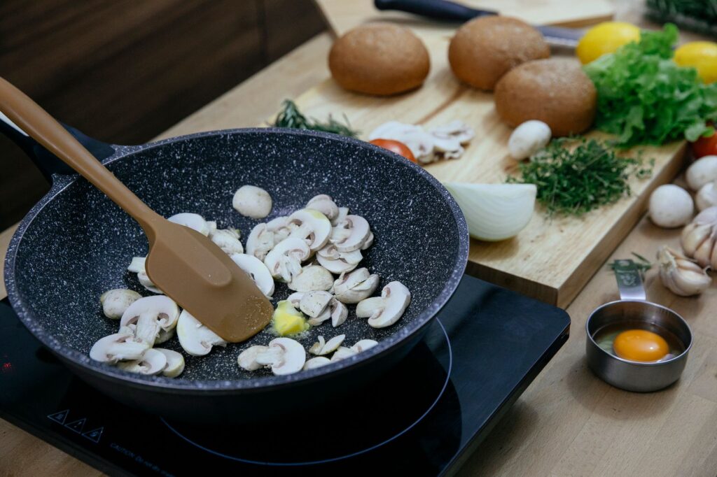 Une scène de cuisine avec des champignons sautés dans une poêle entourés d'ingrédients frais sur une planche à découper.