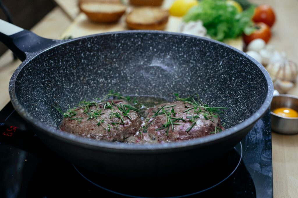 Délicieuses galettes de boeuf cuites avec du romarin frais dans une poêle. Parfait pour les passionnés de cuisine.
