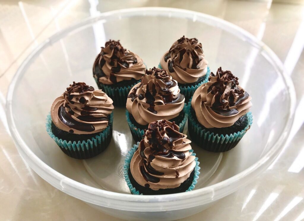 Six délicieux cupcakes au chocolat avec un glaçage au chocolat dans un conteneur en plastique rond.