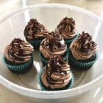 Six délicieux cupcakes au chocolat avec un glaçage au chocolat dans un conteneur en plastique rond.