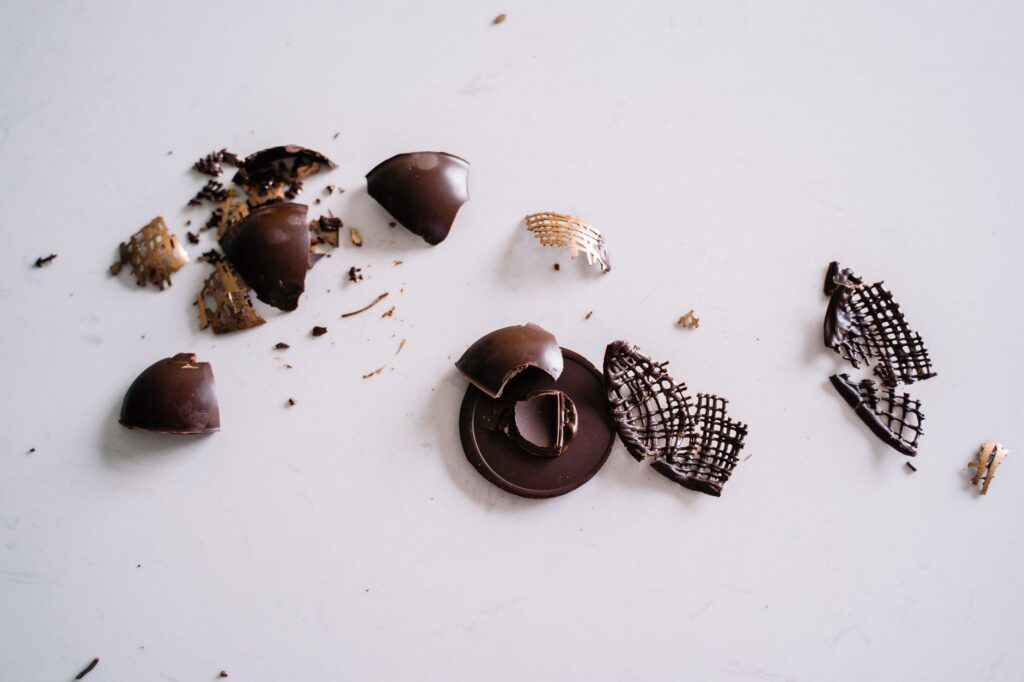 Gros plan sur des morceaux de chocolat noir cassé éparpillés sur une surface blanche lisse. Idéal pour la photographie culinaire et les thèmes de desserts.