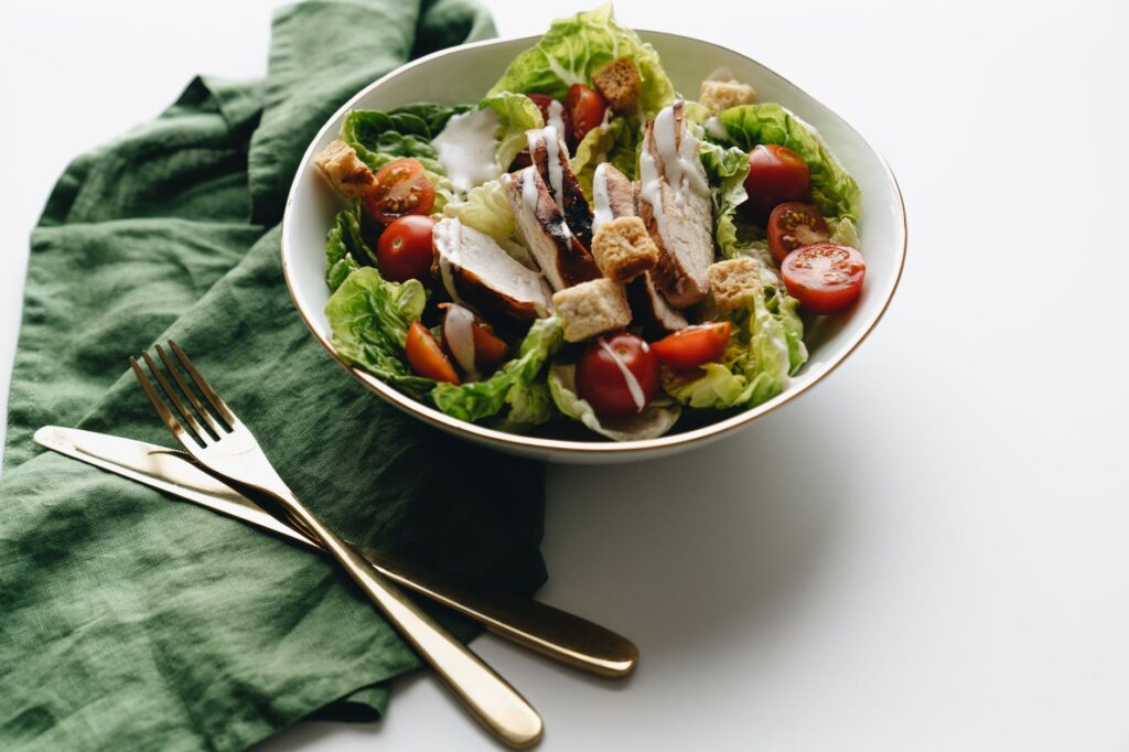 Délicieuse salade César avec poulet grillé, laitue fraîche et tomates cerises sur une assiette blanche.