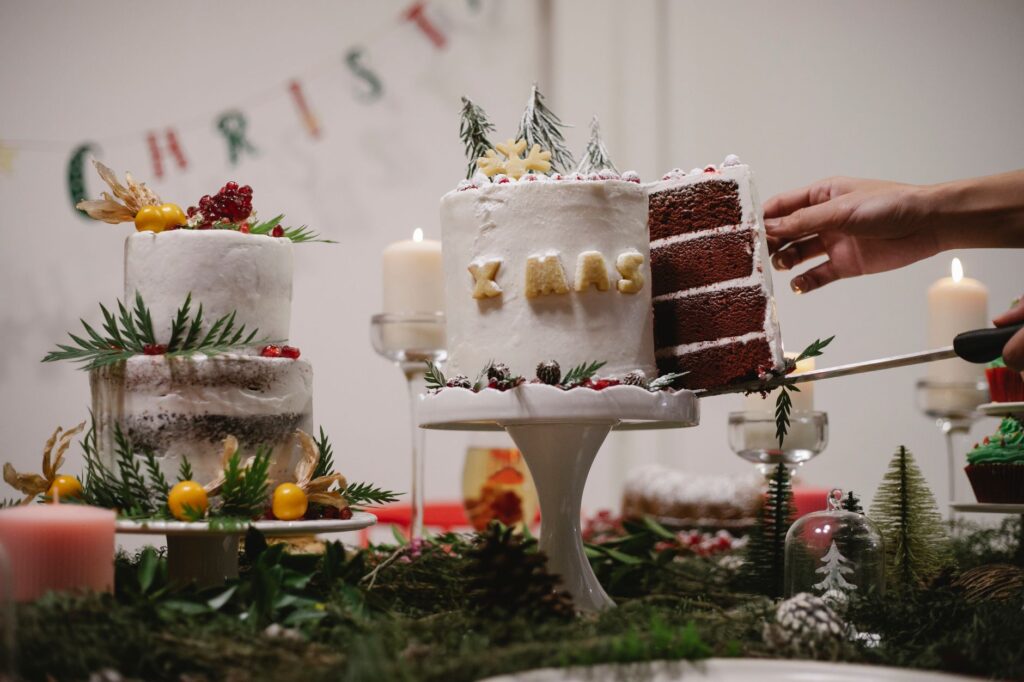 Une main coupe une part d'un gâteau de Noël magnifiquement décoré, orné de décorations festives à l'intérieur.