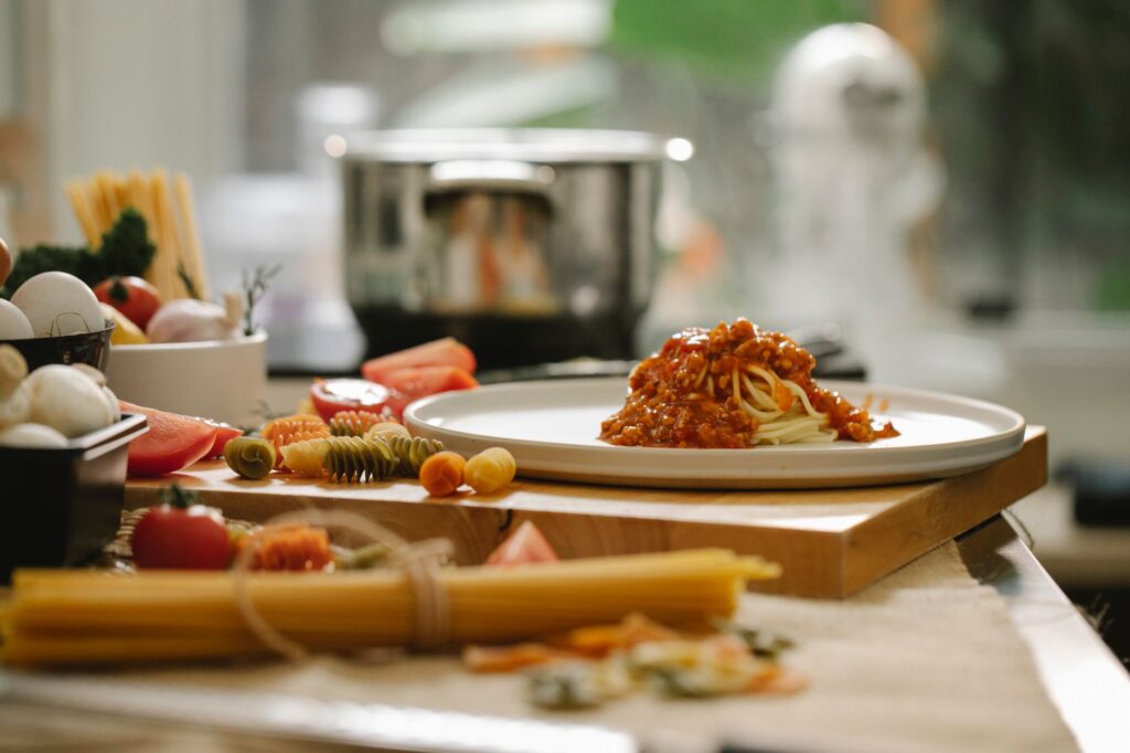 Pasta bolognaise appétissante servie sur une assiette en céramique, entourée d'ingrédients frais dans une cuisine moderne.