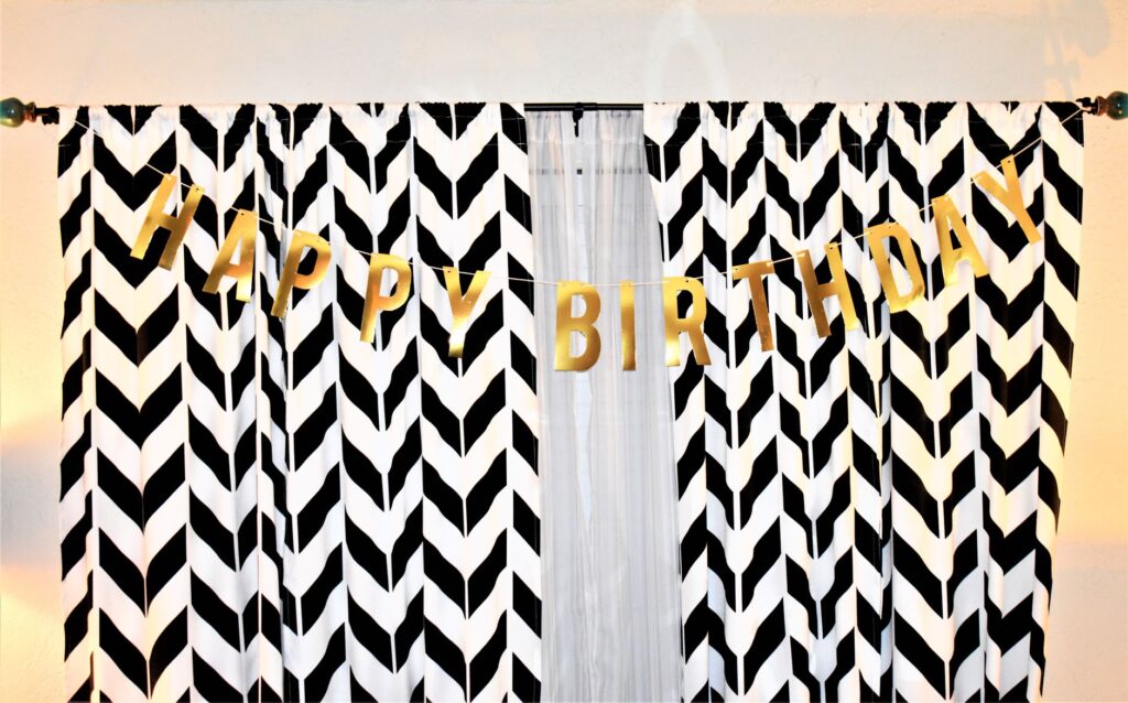 Une joyeuse bannière Joyeux Anniversaire en lettres dorées suspendue sur des rideaux chevrons noir et blanc.