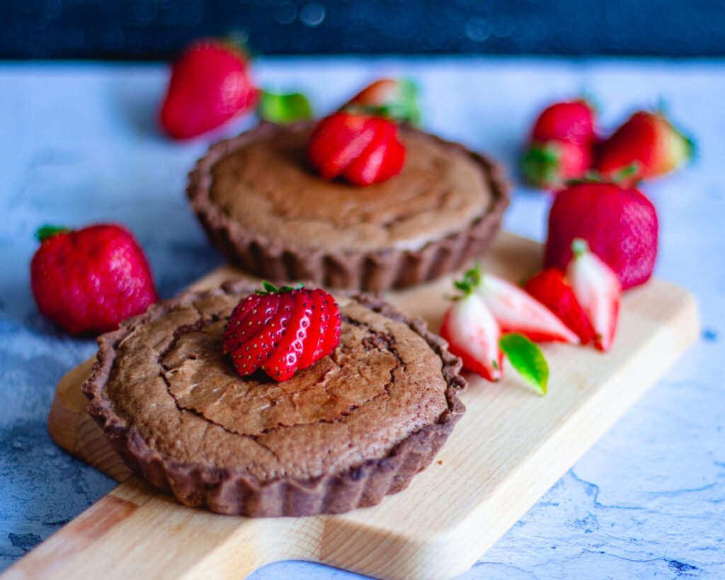 Gros plan sur des tartes au chocolat garnies de fraises sur une planche en bois.