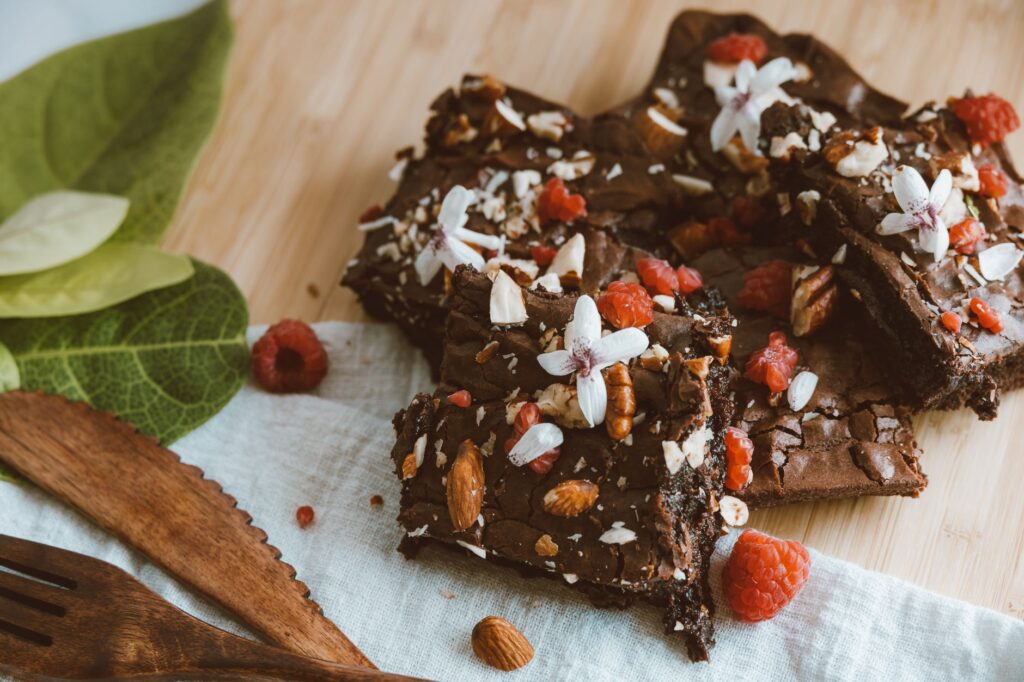Riches brownies au chocolat garnis de framboises, noix et fleurs sur une table en bois.