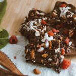 Riches brownies au chocolat garnis de framboises, noix et fleurs sur une table en bois.