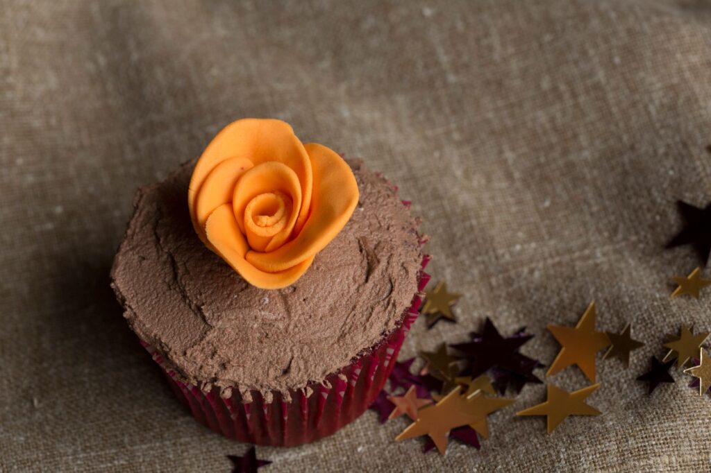 Cupcake au chocolat garni d'une rose orange artificielle et entouré de paillettes en forme d'étoile.