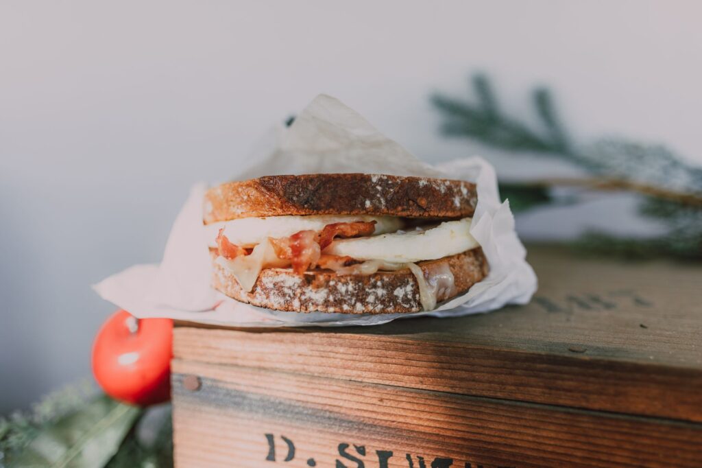 Gros plan sur un sandwich bacon et œuf sur pain au levain, présenté sur une boîte en bois.