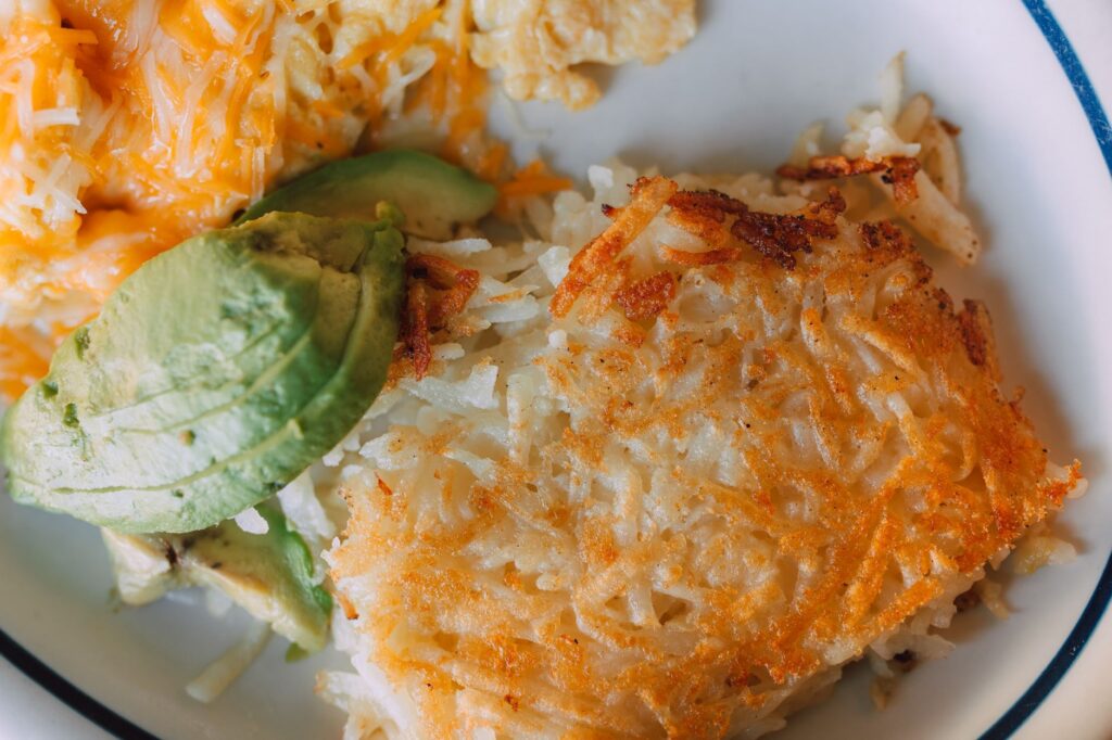 Gros plan sur un petit-déjeuner végétalien avec des tranches d'avocat, des pommes de terre rissolées croustillantes et des œufs brouillés au fromage.