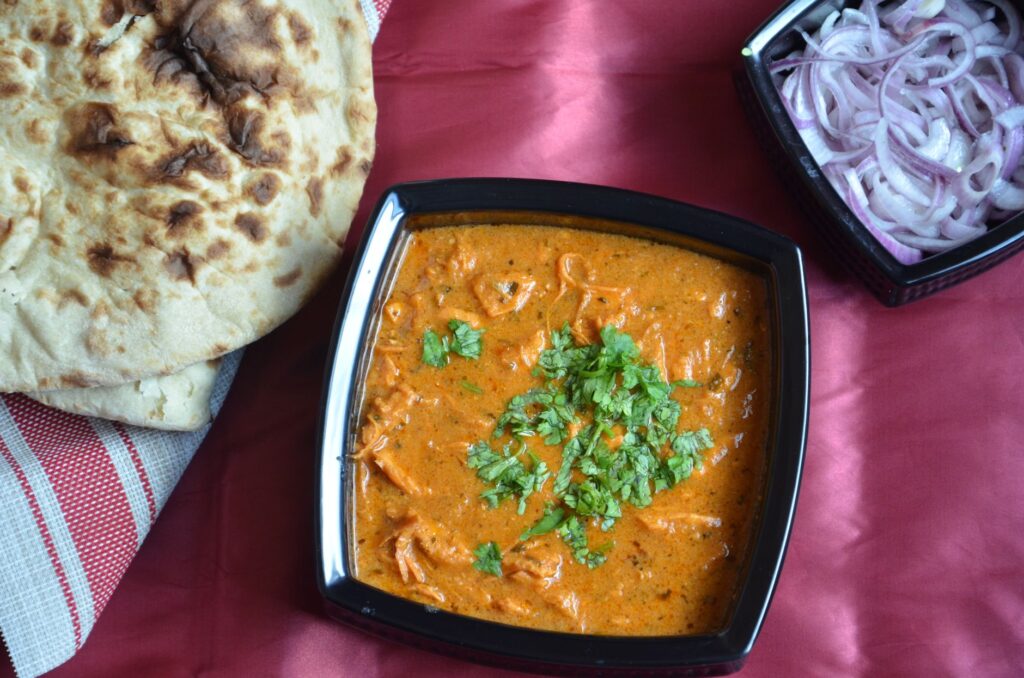 Vue de dessus de curry indien garni de coriandre, servi avec du naan et des oignons.