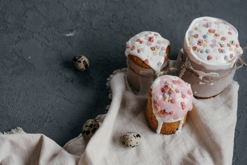 Gâteaux de Pâques décorés de glaçage et de granulés, accompagnés d'œufs de cailles sur un fond en béton texturé.