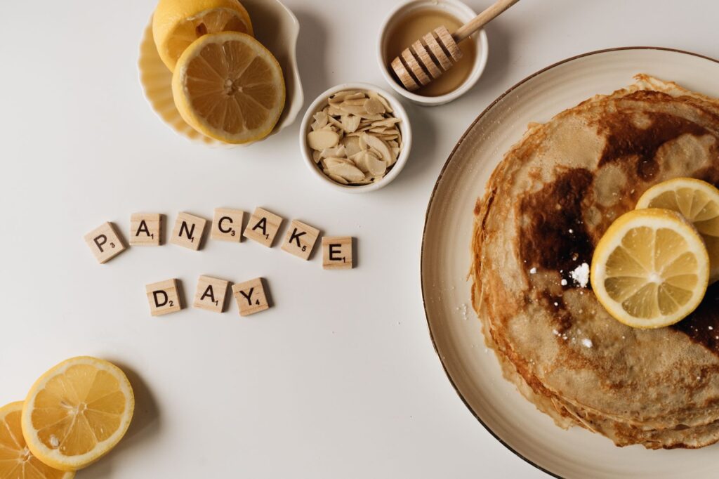 Vue de dessus de crêpes avec des tranches de citron et du miel pour la Journée de la Crêpe, mettant en avant des lettres de Scrabble en bois.