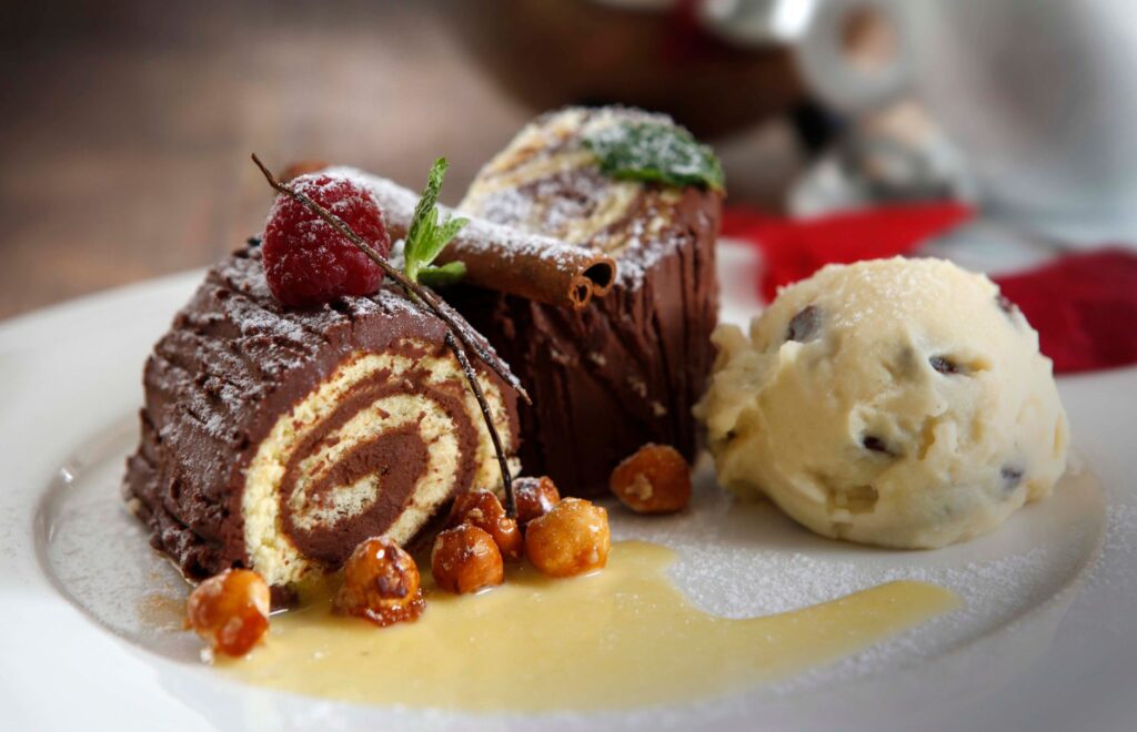 Délicieux roulé au chocolat servi avec de la glace à la vanille et des noix confites sur une assiette en céramique.