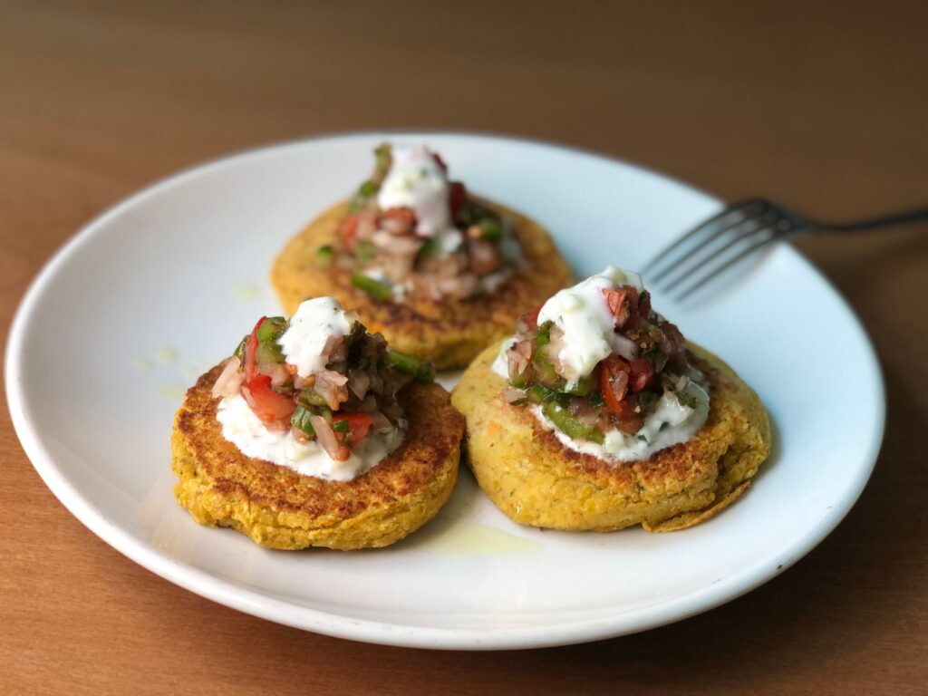 Des beignets de courgette savoureux garnis de salsa fraîche et de yaourt sur une assiette en céramique.