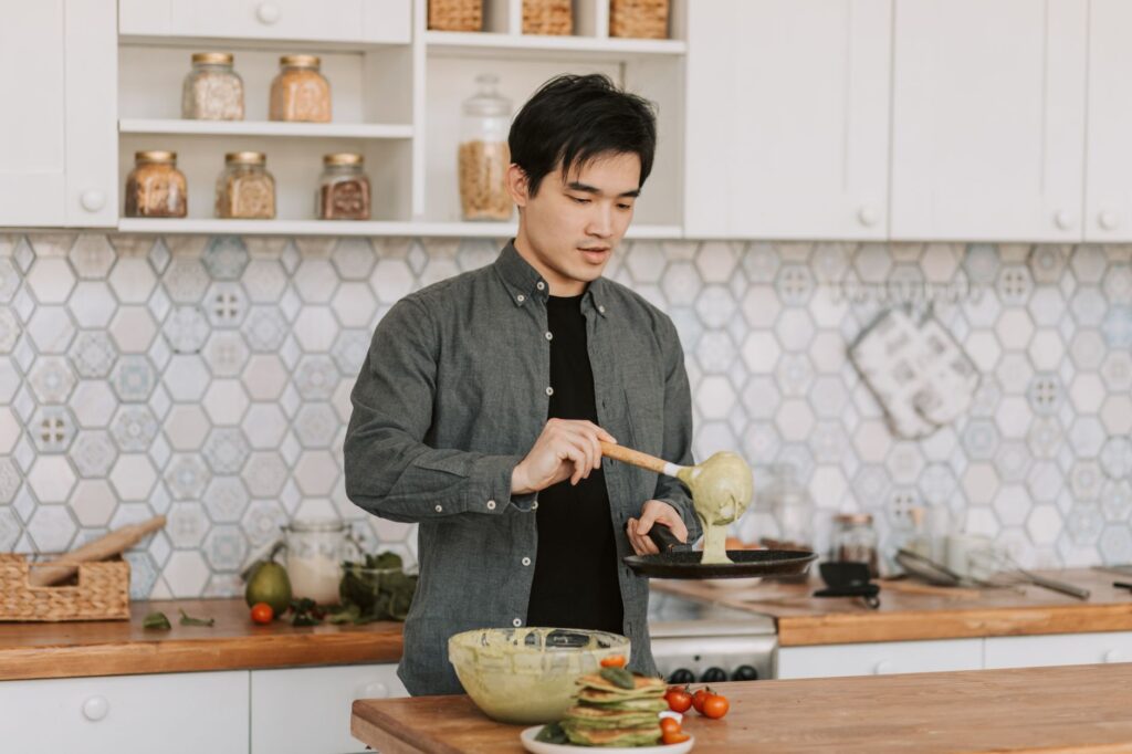 Un jeune homme cuisinant des crêpes dans une cuisine élégante, mettant en avant ses compétences culinaires.